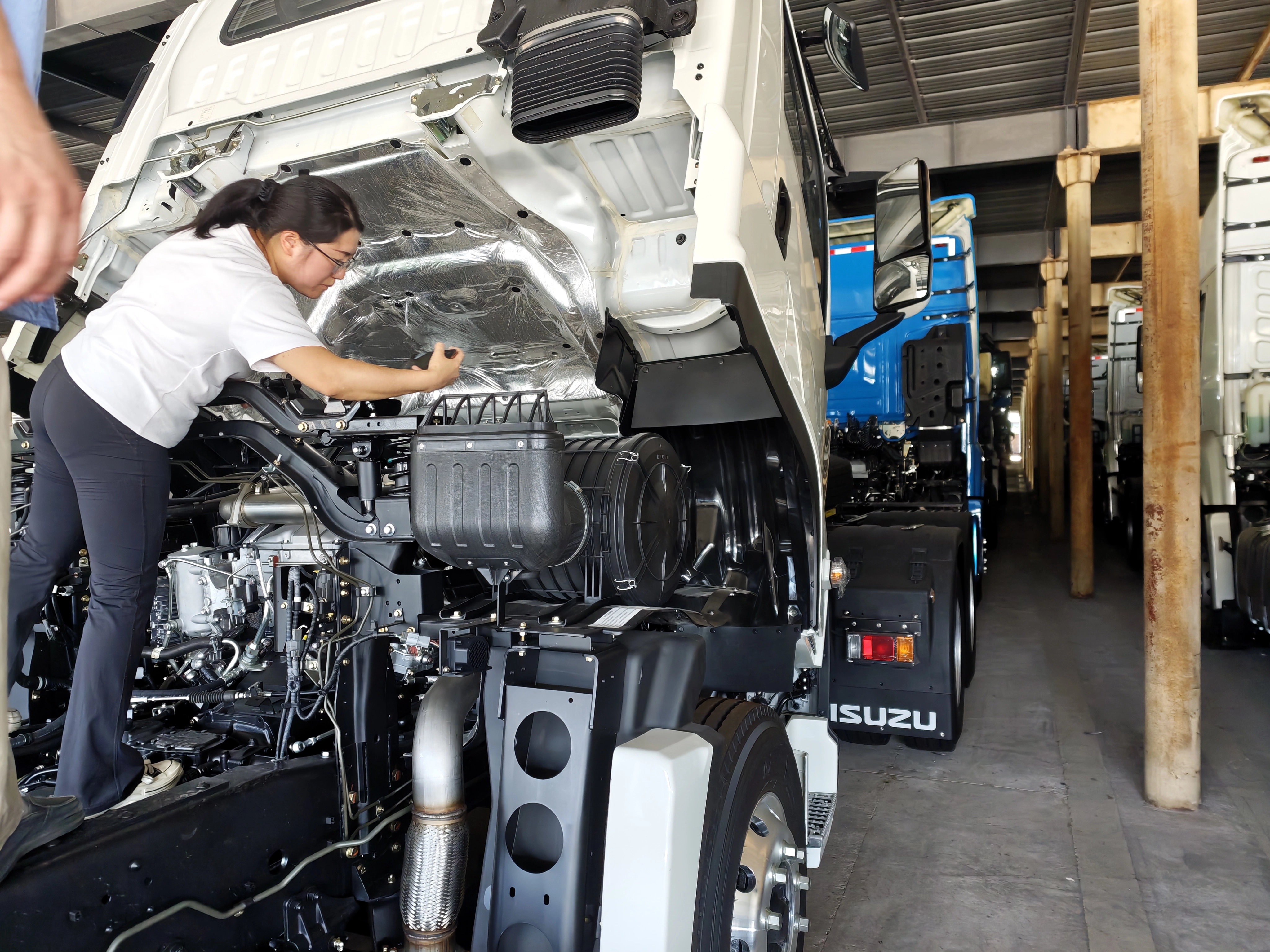 Inspector conducting detailed engine compartment inspection on ISUZU truck before shipment to Peru.